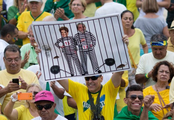 In this March 13, 2016 file photo, a demonstrator holds a poster with the photo of Brazilian president Dilma Rousseff and former President Luiz Inacio Lula da Silva in prison stripes during a protest on Copacabana beach in Rio de Janeiro, Brazil. It was the best of times in 2009 when Rio was awarded the games, championed by then-President Luiz Inacio Lula da Silva. He called it a "sacred day" and praised the "strength of Brazil's economy," which shrank by 4 percent in 2015 with no improvement in sight. (AP Photo/Silvia Izquierdo, File)